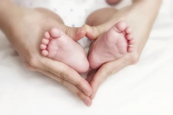 Neugeborene Babyfüße in den Händen der Mutter lizenzfreie Stockbilder