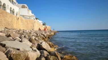 Hammamet, Tunus - 26 Ağustos 2022: Medine 'nin önünde denizin tadını çıkaran insanlar. Şehir yüzme ve su sporları için popüler bir yerdir ve Tunus 'un en önemli noktalarından biridir..