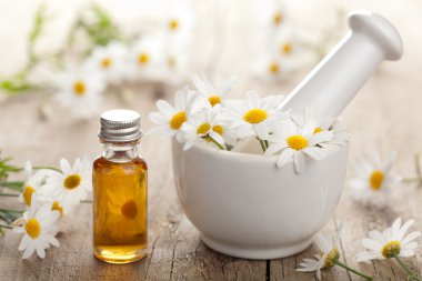 essential oil and camomile flowers in mortar clipart