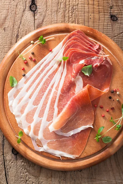 Sliced prosciutto ham on chopping board with oregano and pepper — Stock Photo, Image