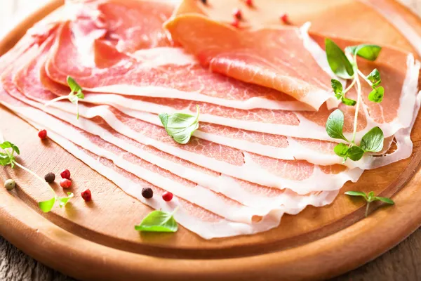 Sliced prosciutto ham on chopping board with oregano and pepper — Stock Photo, Image