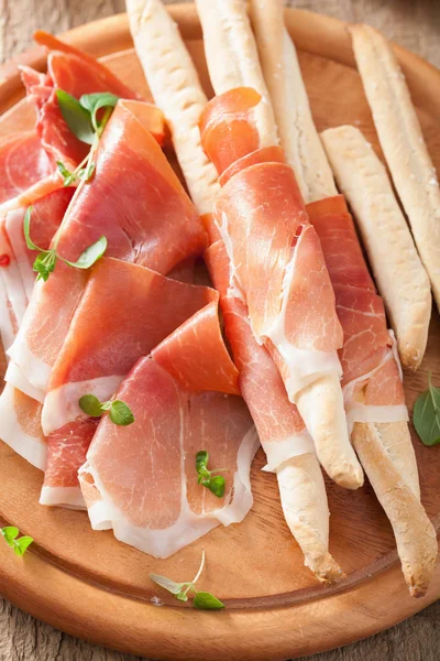 Sliced prosciutto ham and grissini bread sticks — Stock Photo, Image