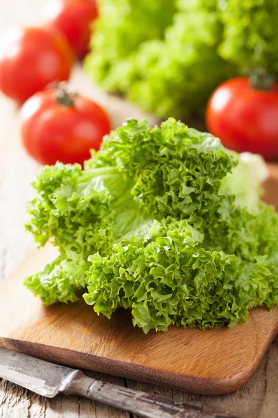 Fresh lollo leaves and tomatoes on chopping board for salad — Stock Photo, Image