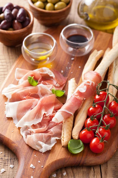 Italian prosciutto ham grissini bread sticks tomato olive oil — Stock Photo, Image
