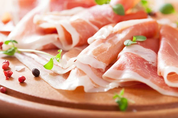 Sliced prosciutto ham on chopping board with oregano and pepper — Stock Photo, Image