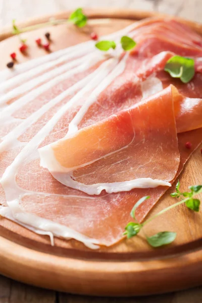 Sliced prosciutto ham on chopping board with oregano and pepper — Stock Photo, Image