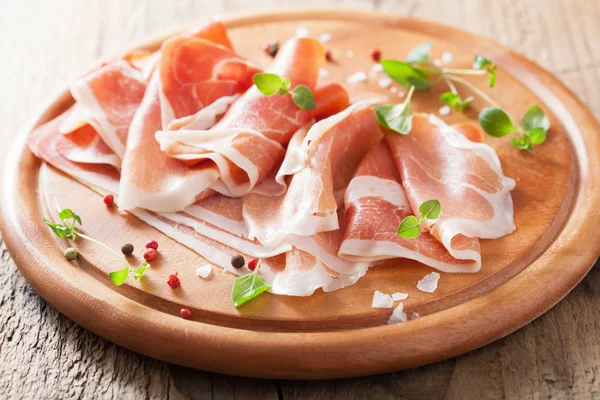 Sliced prosciutto ham on chopping board with oregano and pepper — Stock Photo, Image