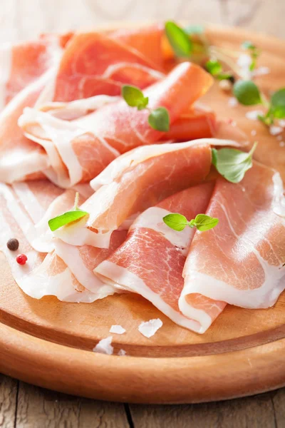 Sliced prosciutto ham on chopping board with oregano and pepper — Stock Photo, Image