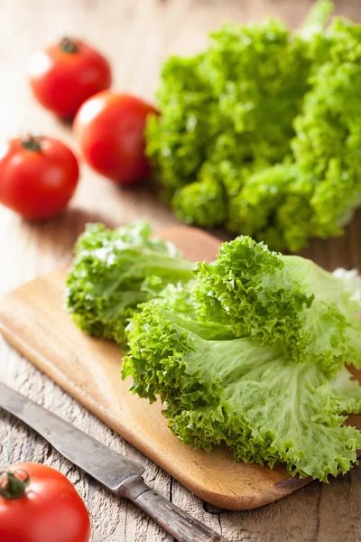 Fresh lollo leaves and tomatoes on chopping board for salad — Stock Photo, Image