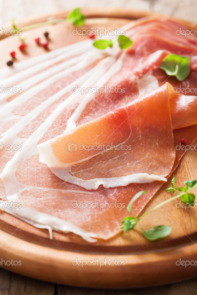 sliced prosciutto ham on chopping board with oregano and pepper 