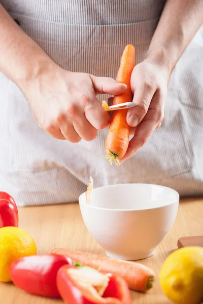 Homem descascando cenoura na cozinha — Fotografia de Stock