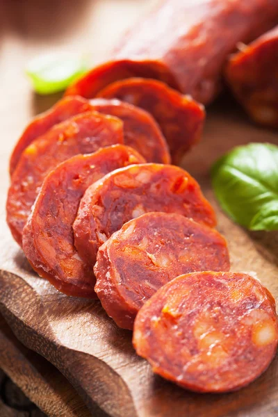 Spanish chorizo sausage with basil on chopping board — Stock Photo, Image