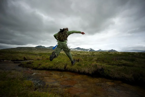 Homem caminhante saltando através de rio pequeno — Fotografia de Stock