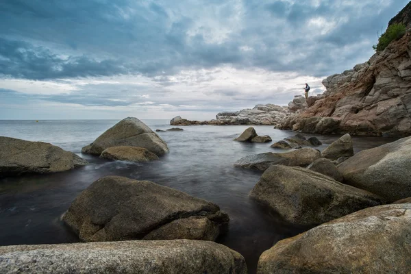 La silhouette dell'uomo sulla spiaggia rocciosa — Foto Stock