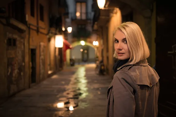 Beautiful blond woman in raincoat walking alone outdoors at night — Stock Photo, Image