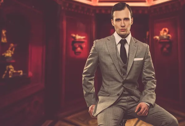 Confident man in classic grey suit sitting on chair in cabinet — Stock Photo, Image