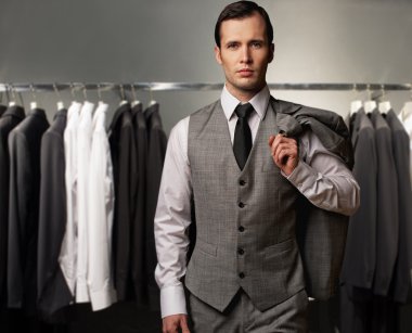 Businessman in classic vest against row of suits in shop clipart