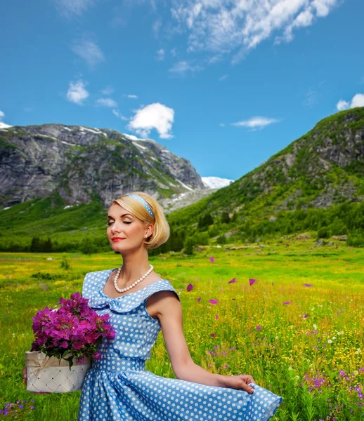 Прекрасна жінка в блакитній сукні з кошиком квітів на тлі краєвиду гори — стокове фото