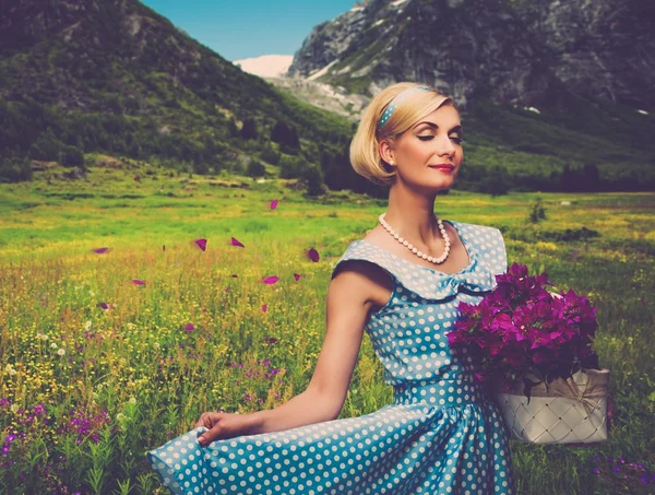 Lovely woman in blue dress with basket of flowers against mountain view Royalty Free Stock Photos