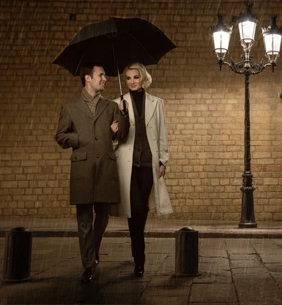 Elegant couple with umbrella outdoors on rainy evening — Stock Photo, Image