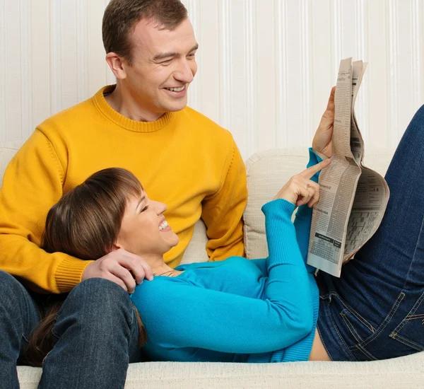 Glad ung man och kvinna med tidningen på soffan i heminredning — Stockfoto