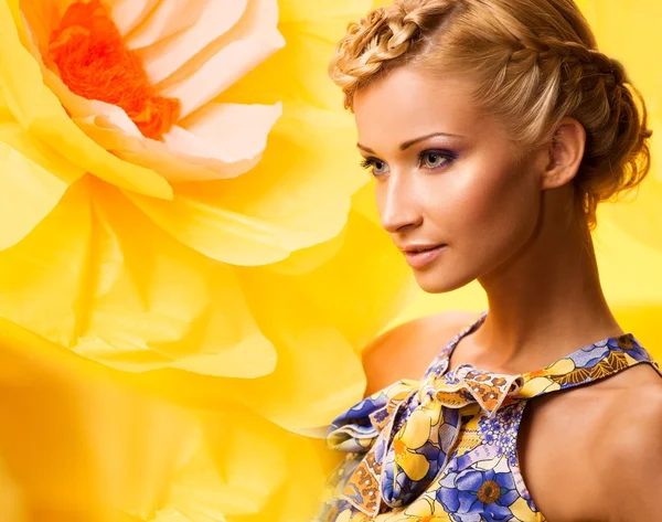 Beautiful young cheerful blond woman in colourful dress among big yellow flowers — Stock Photo, Image