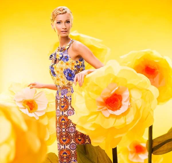 Belle jeune femme blonde en robe colorée parmi les grandes fleurs jaunes — Photo
