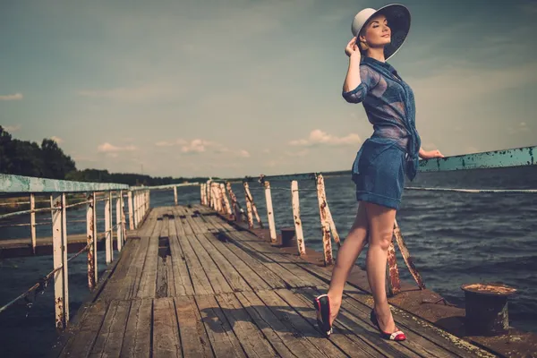 Stylish woman in white hat standing on old wooden pier — Stock Photo, Image