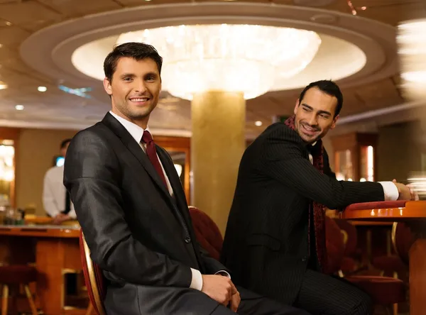 Two young men in suits behind table in a casino — Stock Photo, Image