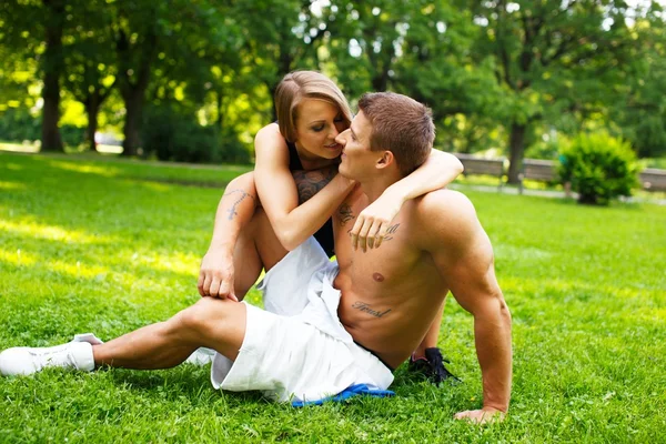 Joven feliz sonriente pareja deportiva sentada en un prado en un parque — Foto de Stock