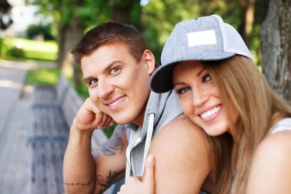 Jovem feliz sorrindo casal desportivo sentado no banco em um parque — Fotografia de Stock