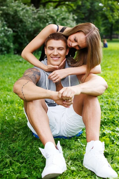 Jovem feliz sorrindo casal desportivo sentado em um prado em um parque — Fotografia de Stock
