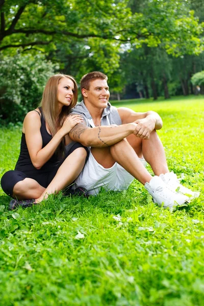 Casal desportivo sentado em um prado em um parque — Fotografia de Stock