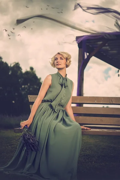 Woman in long green dress sitting on a bench — Stock Photo, Image