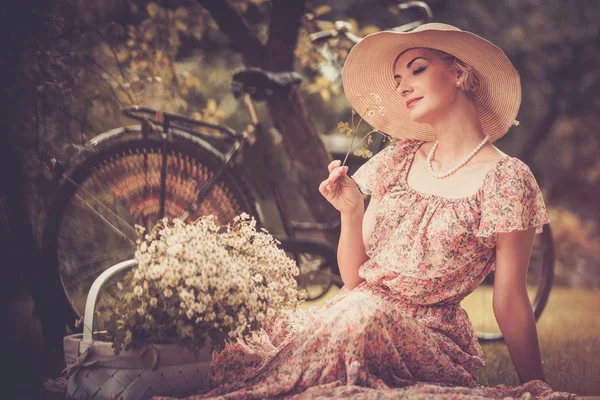 Retro woman with basket of flowers n and bicycle — Stock Photo, Image