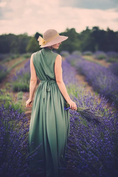 Žena v dlouhé zelené šaty a klobouk v poli levandule — Stock fotografie