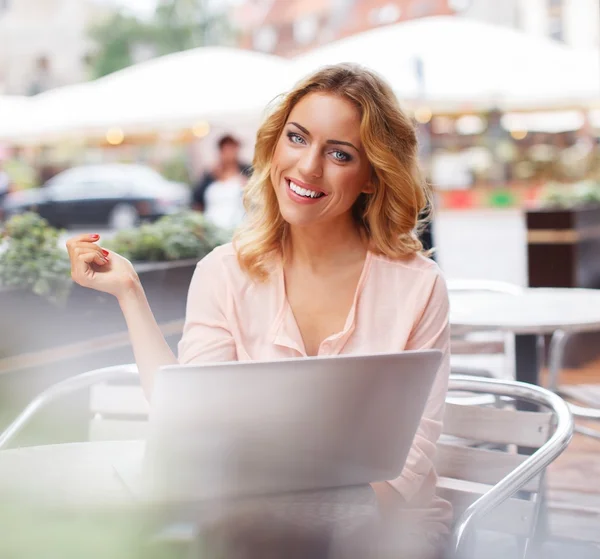 Smiling young woman alone with laptop in summer cafe — Stock Photo, Image