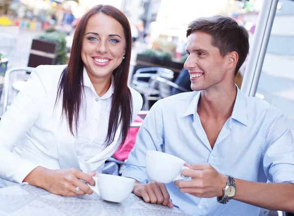 Молодая пара с чашками сидя в летнем кафе — стоковое фото
