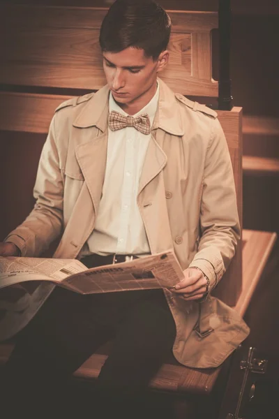 Handsome young man in coat reading newspaper inside vintage train coach — Stock Photo, Image