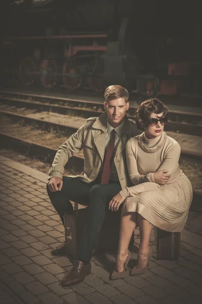 Bonito casal estilo vintage sentado em malas na plataforma da estação ferroviária — Fotografia de Stock