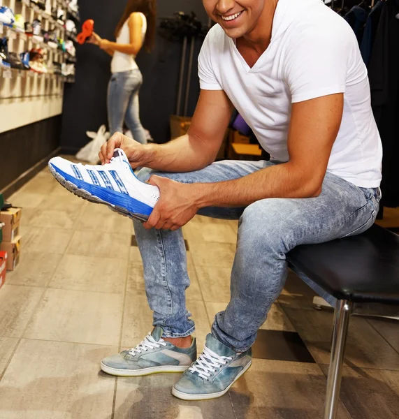 Молодой красивый мужчина выбирает спортивную обувь в спортивной розетке — стоковое фото