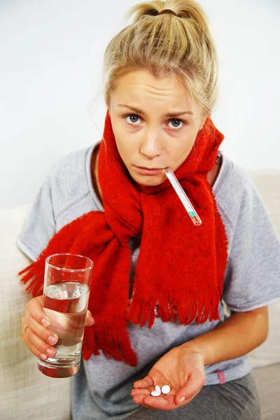 Doente jovem loira com pílulas, termômetro e copo de água — Fotografia de Stock