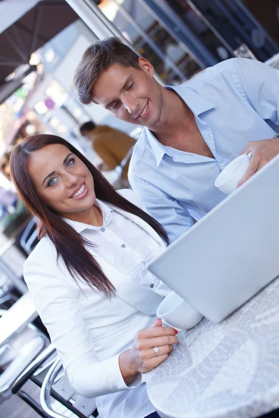 Young couple with cups and laptop in summer cafe — Stock Photo, Image