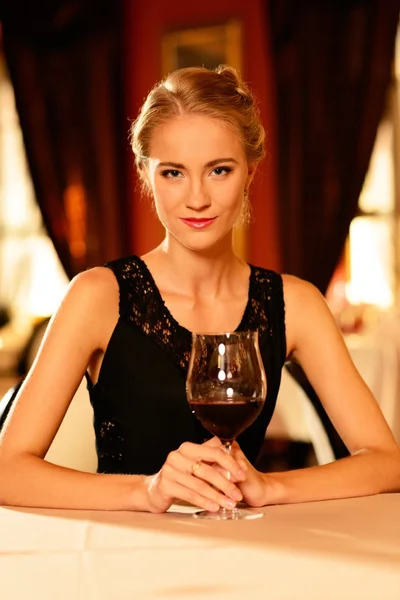 Hermosa joven con copa de vino tinto solo en un restaurante — Foto de Stock