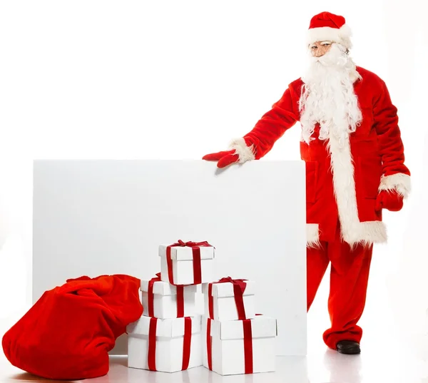 Papai Noel com saco cheio de caixas de presente e placa de aviso em branco — Fotografia de Stock