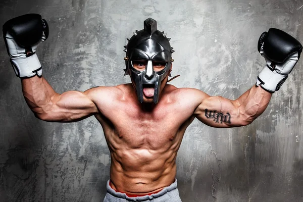 Young man in boxing gloves and gladiator helmet posing — Stock Photo, Image