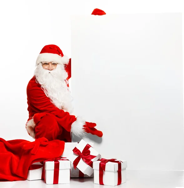 Papai Noel com saco cheio de caixas de presente e placa de aviso em branco — Fotografia de Stock