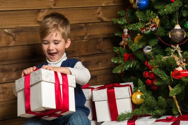 Liten pojke öppna presentförpackning under granen — Stockfoto