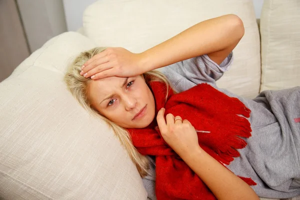 Kranke junge Frau mit Thermometer liegt zu Hause auf Sofa — Stockfoto