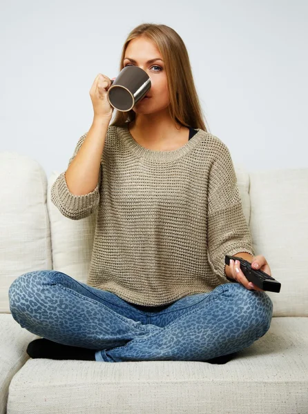 Joven hermosa mujer en un sofá con control remoto y taza — Foto de Stock